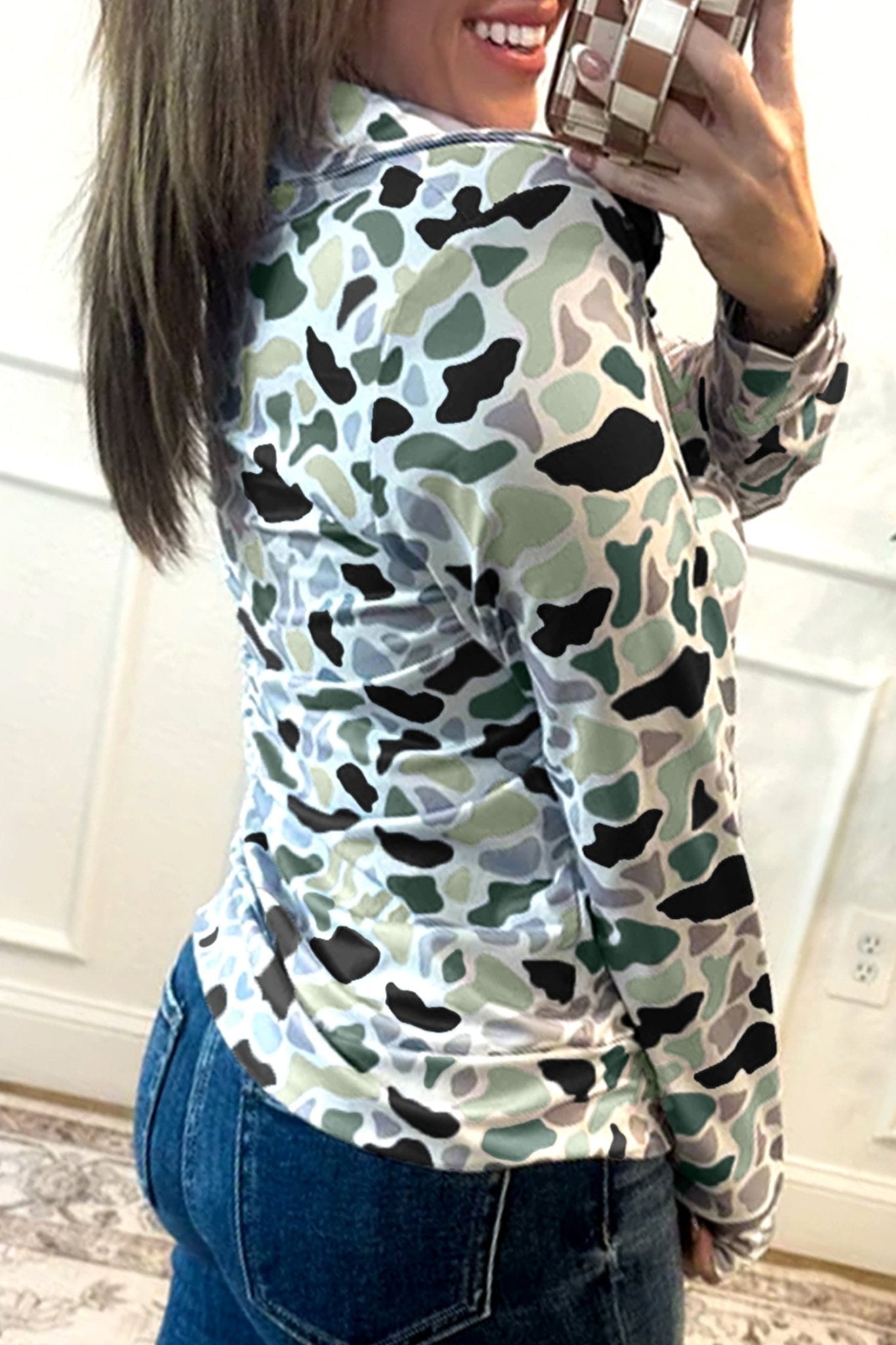 Person wearing a camouflage-patterned shirt in a room with white walls.