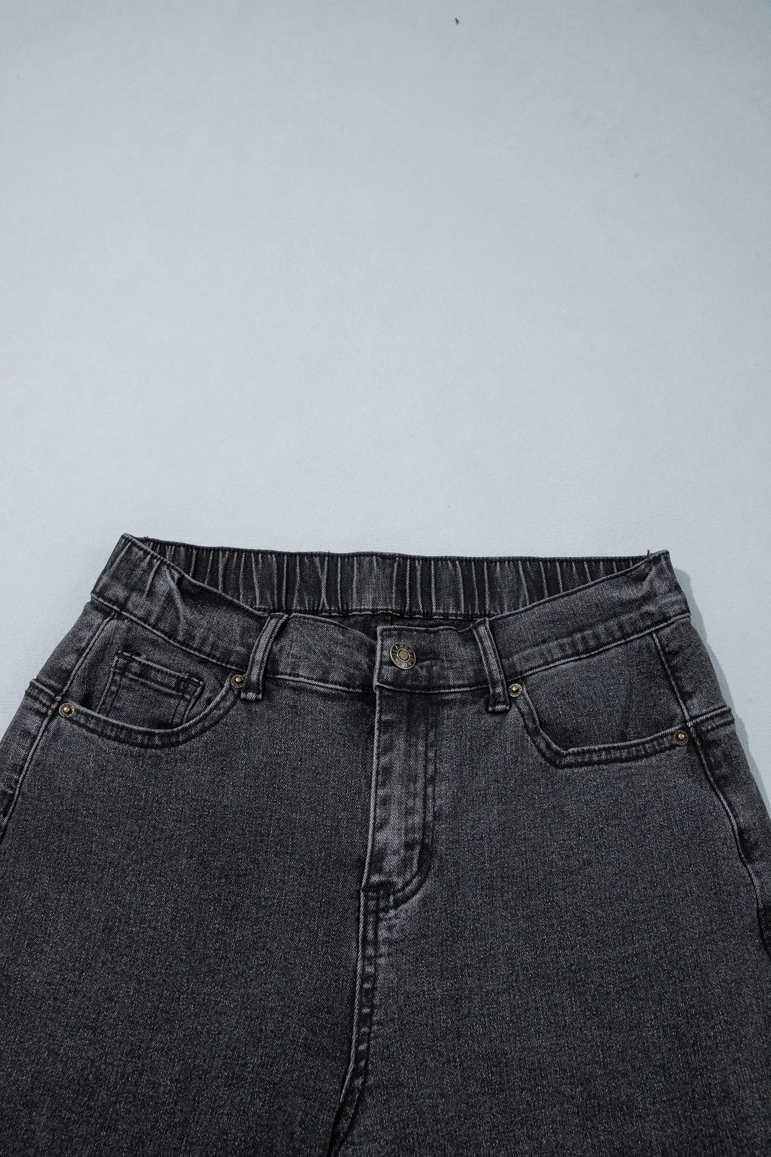 Close-up of waistband, button and pockets on carbon grey jeans