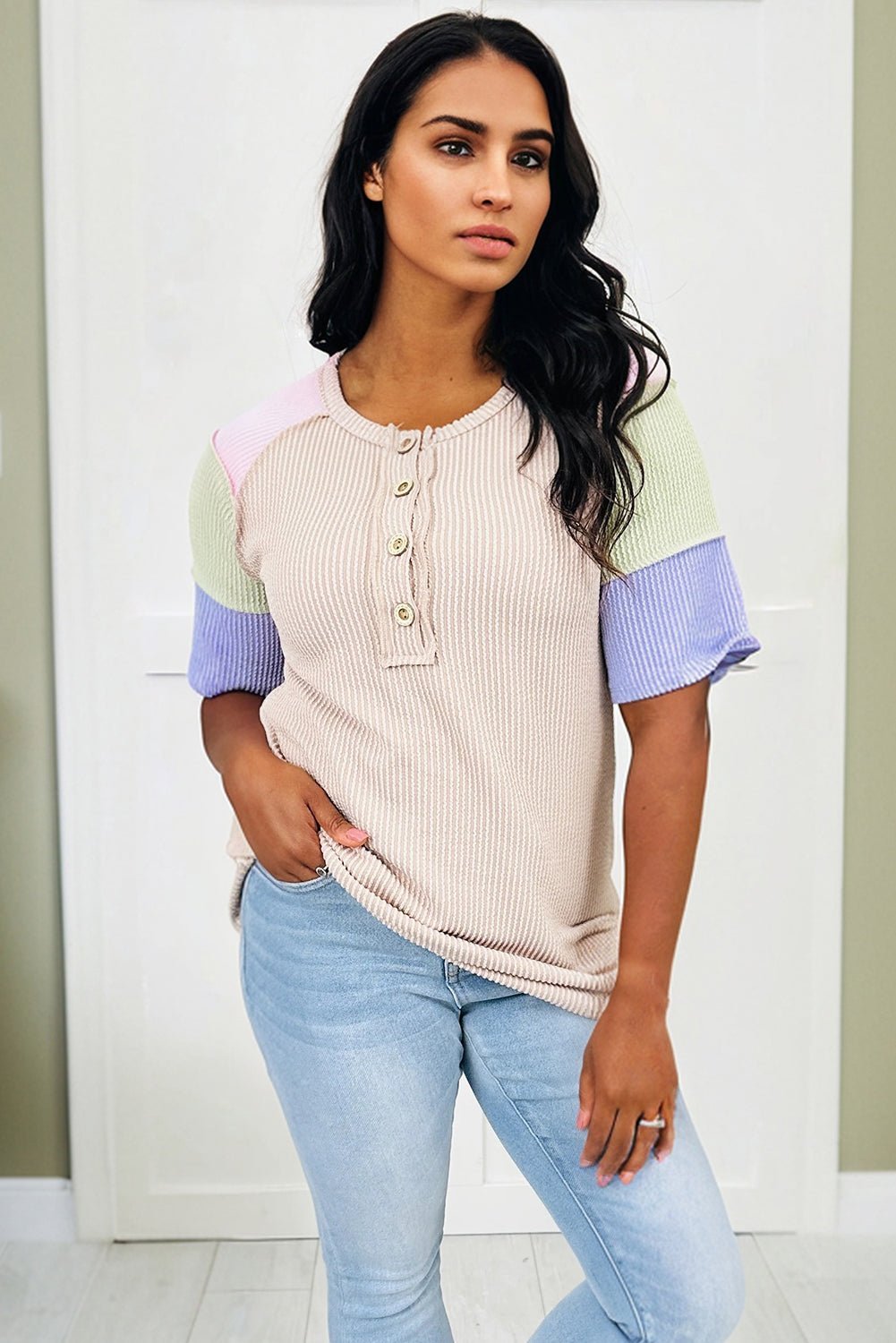 Woman wearing a colorful ribbed sweater and light blue jeans against a white background