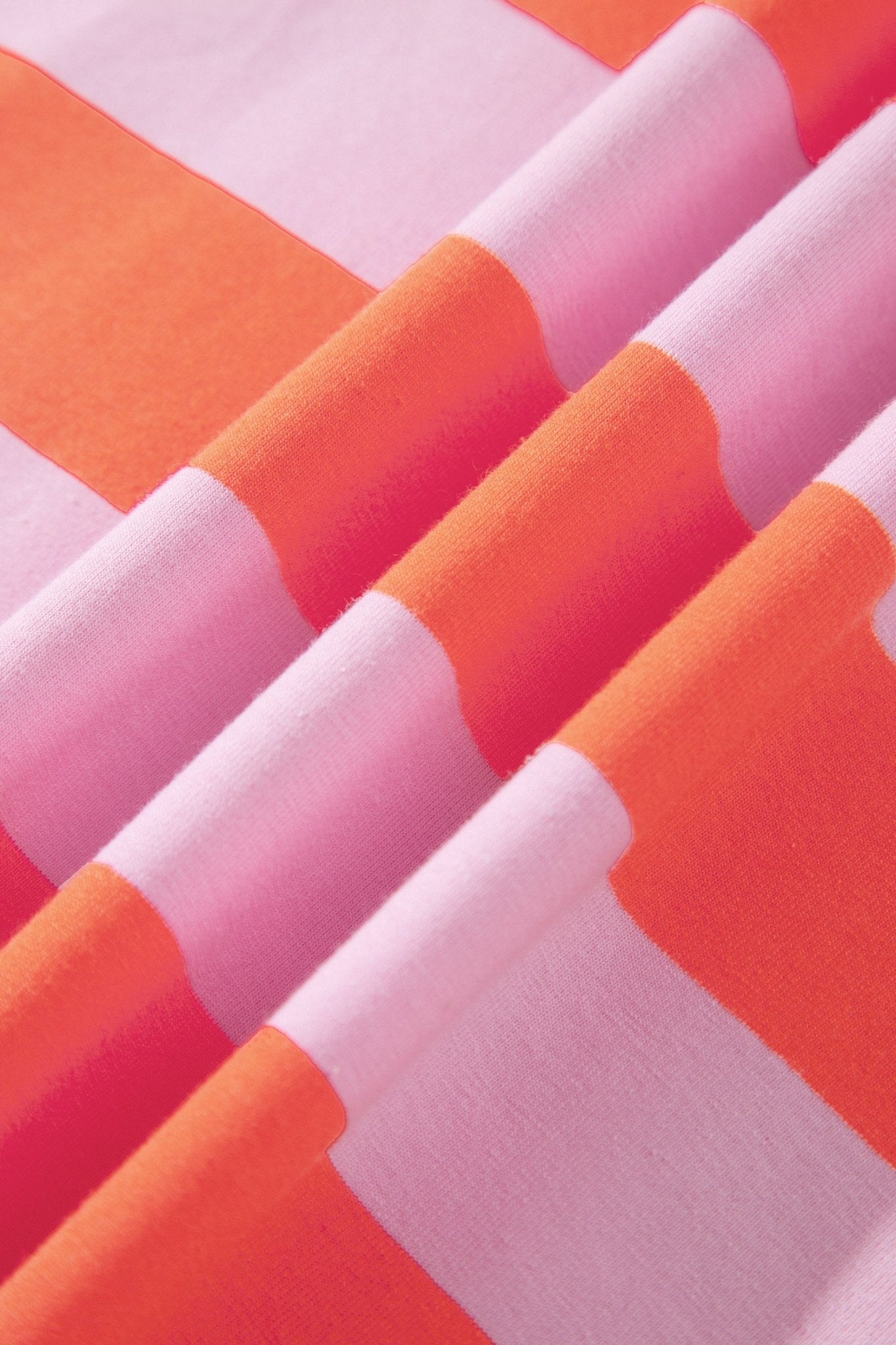 A close-up of draped fabric with bold orange and light pink horizontal stripes.