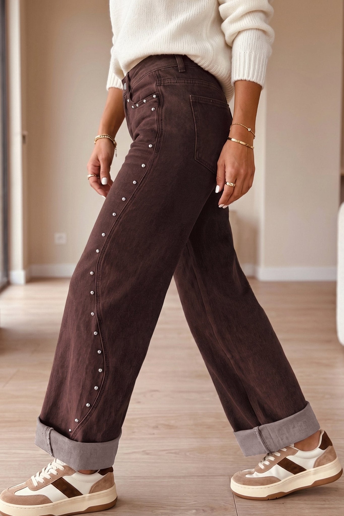 Dark brown wide-leg jeans with silver rivets, cream knit sweater, and brown-white sneakers.