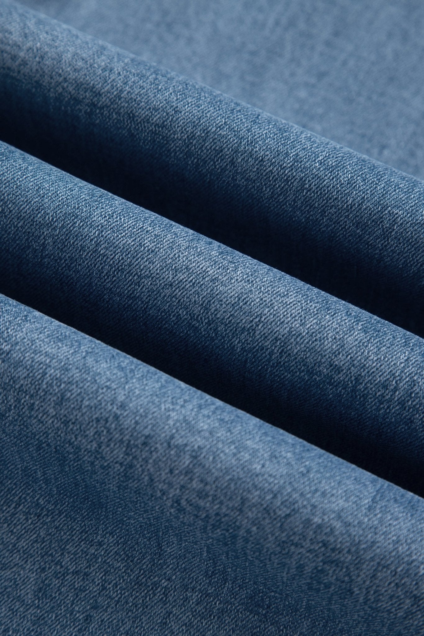 A close-up of folded blue denim fabric showing the textured twill weave and soft shadows between the layers.