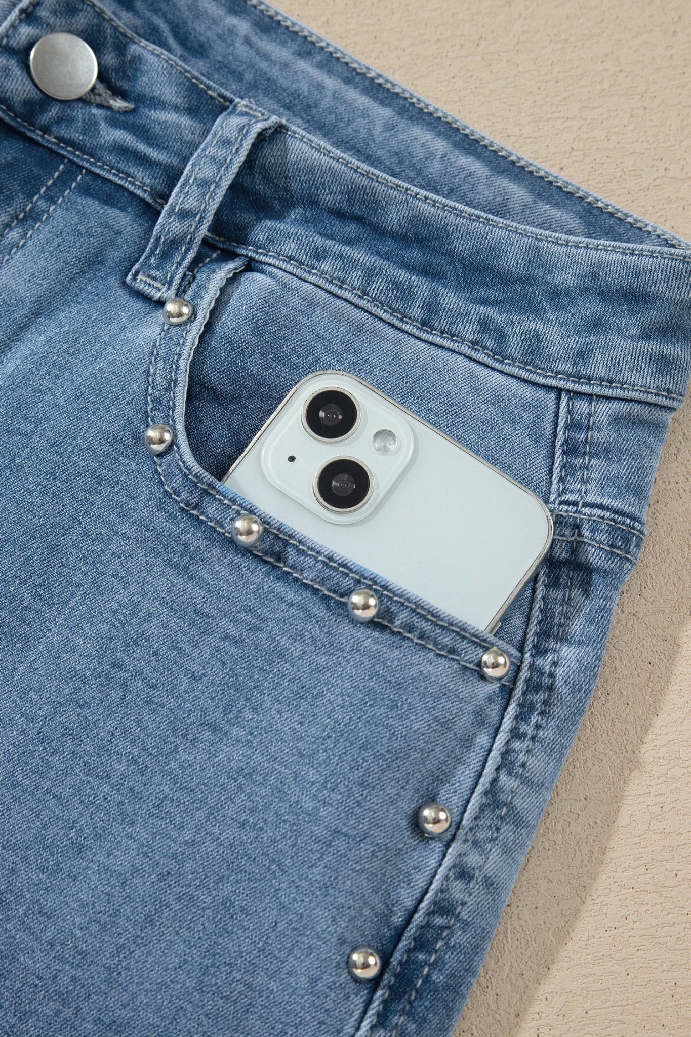 Close-up of light blue denim jacket pocket with silver studs and smartphone.