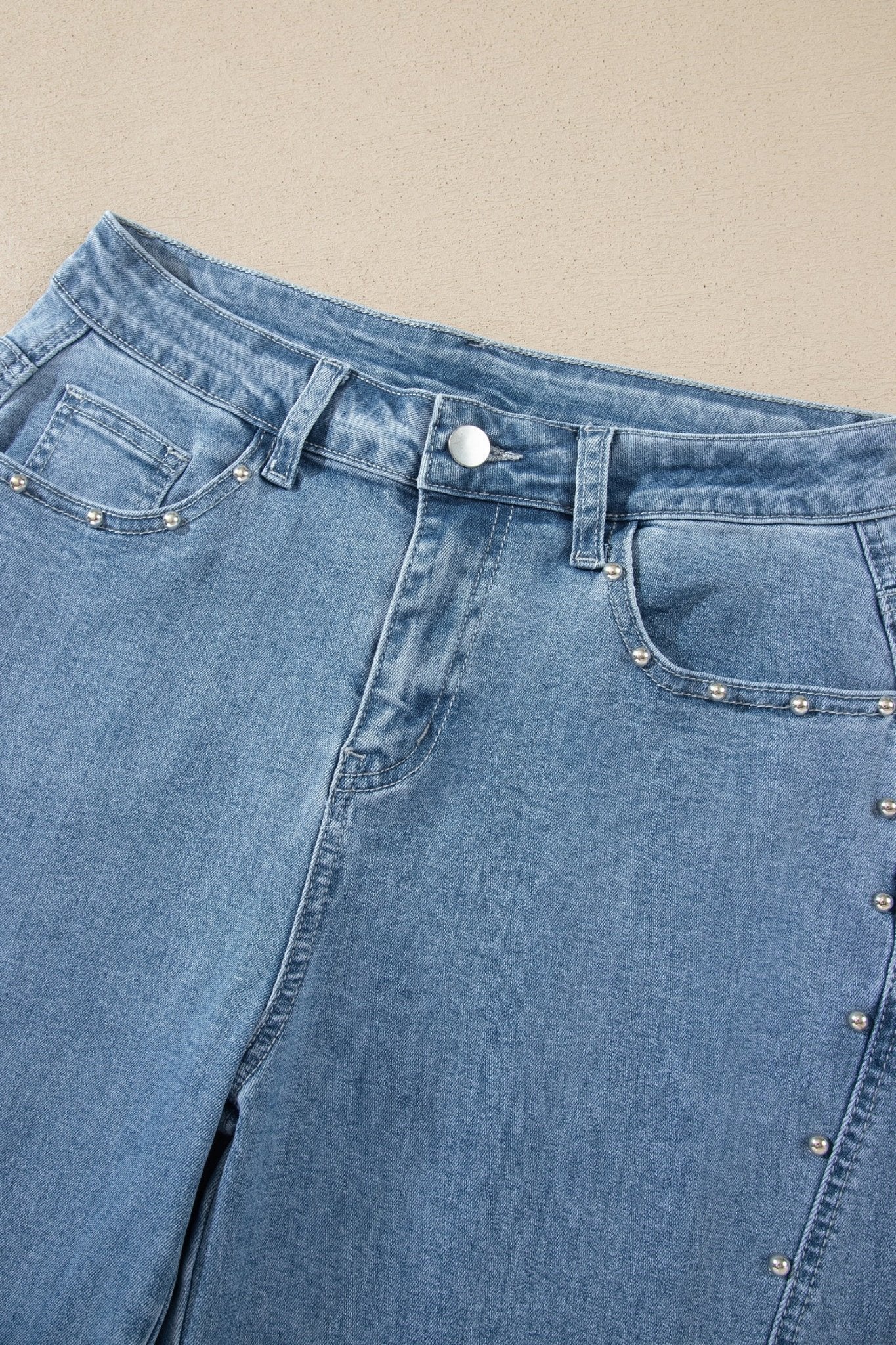 Close-up of light blue jeans with silver studs along the pocket edges.