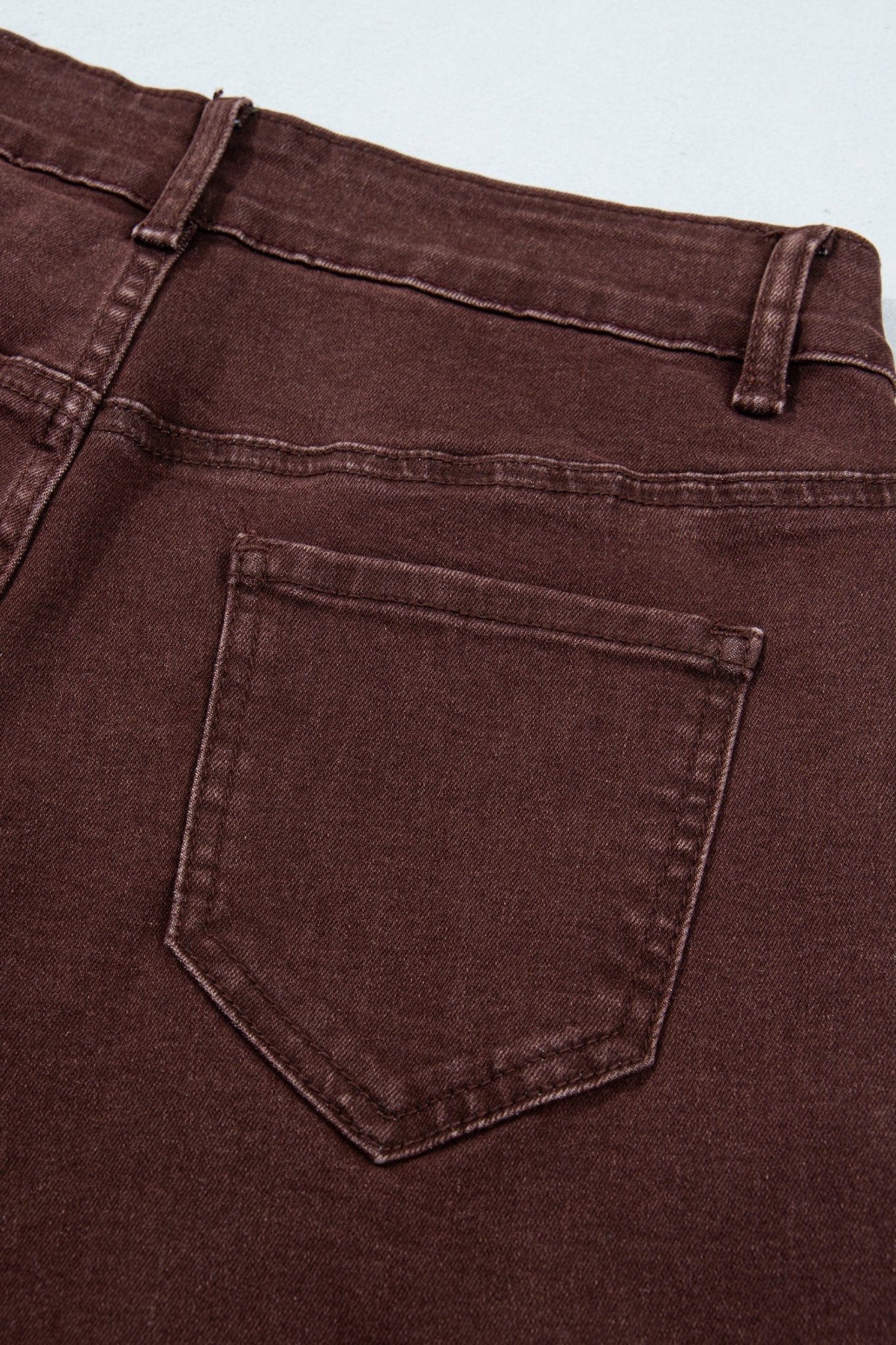 Close-up of dark brown jeans back waistband and pocket with belt loops and stitching.