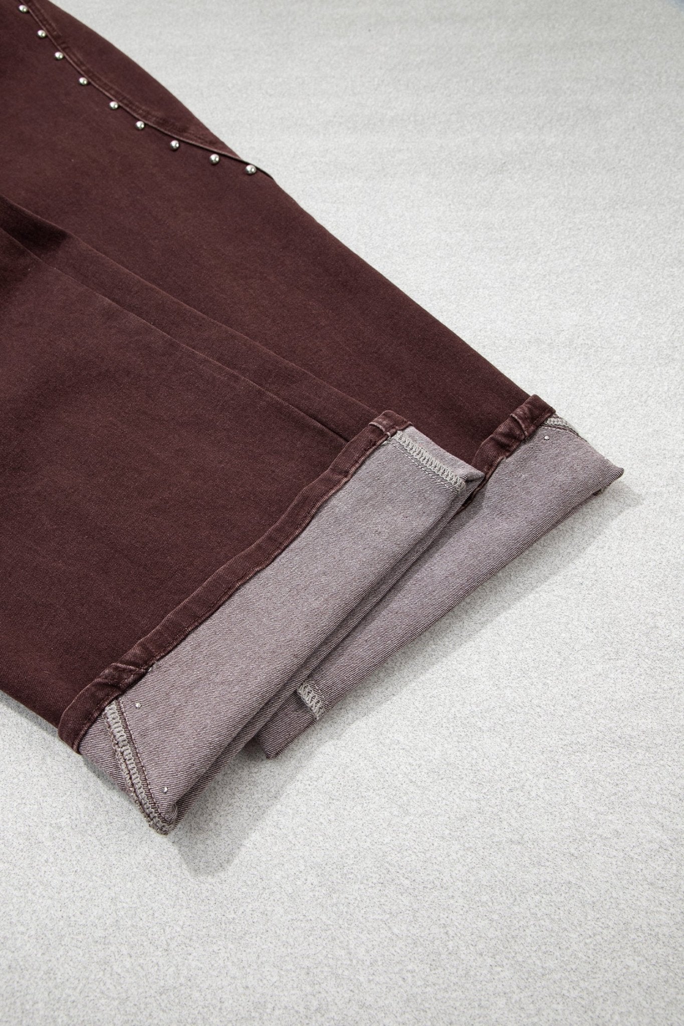 Close-up of folded dark brown pants with gray lining and rolled cuffs.