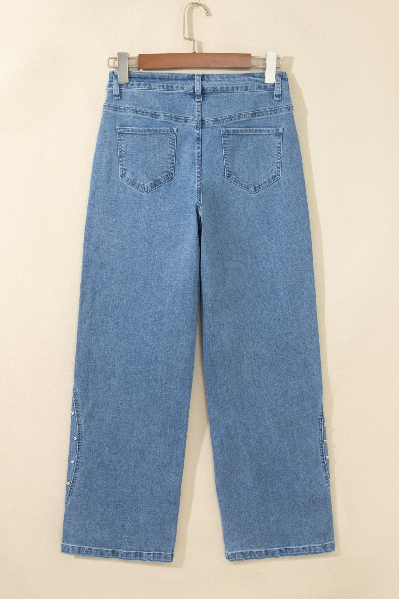 Light blue wide-leg denim jeans shown from the back, hanging on a wooden hanger against a plain beige wall.