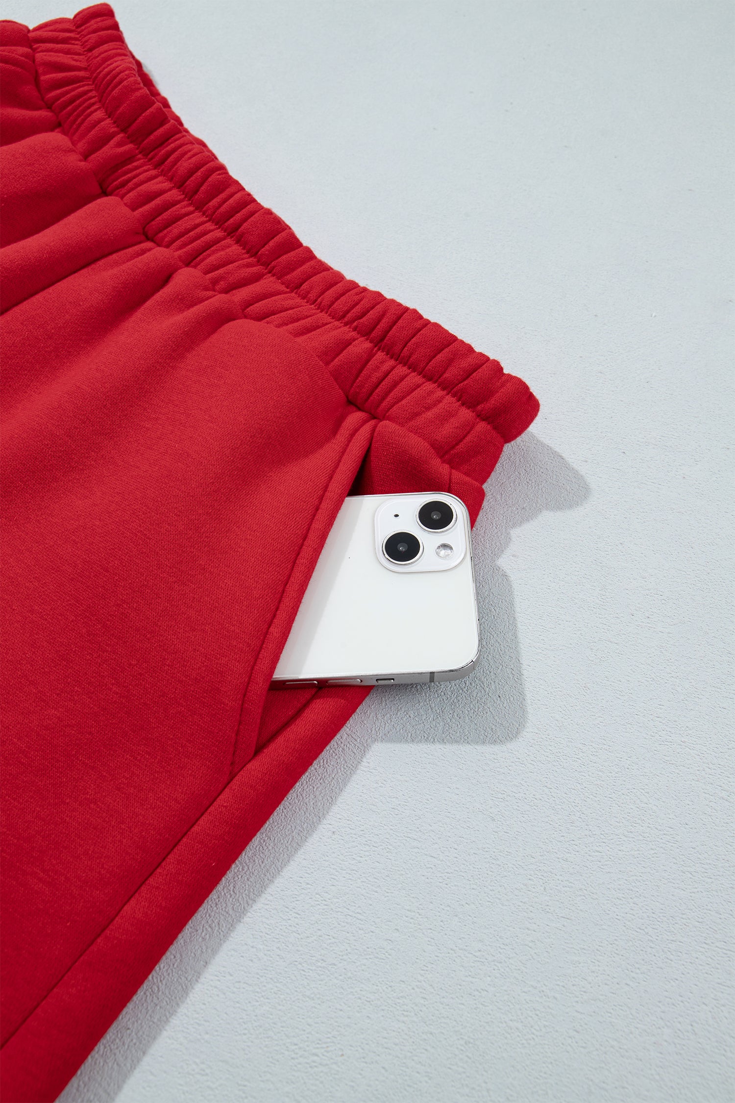 Red sweatpants with an elastic waistband, shown with a white smartphone tucked into the side pocket against a light gray background.