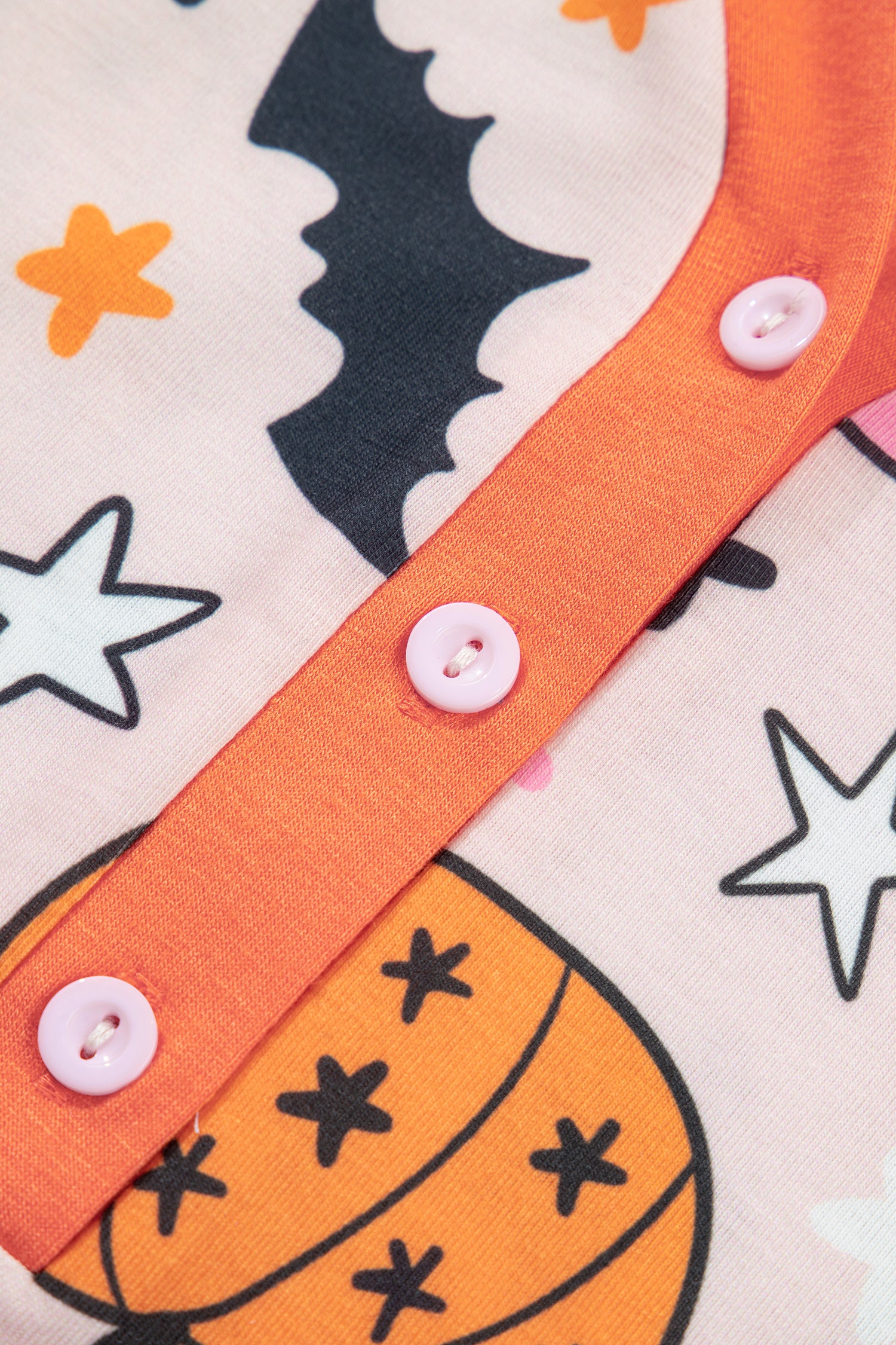Close-up of peach Halloween fabric with bat, pumpkin, orange trim, and pink buttons.
