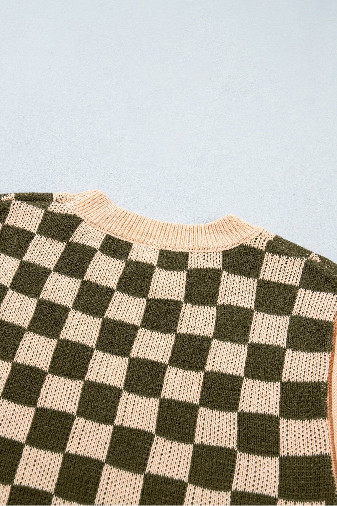 Close-up of dark olive green and cream checkerboard knit sweater with ribbed cream crew neck.