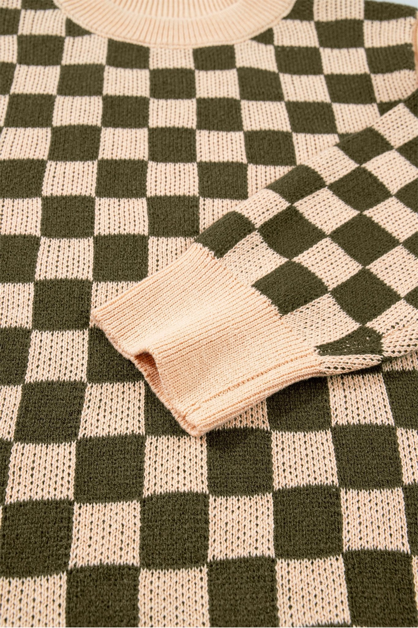 Close-up of dark olive green and cream checkerboard knit sweater featuring a ribbed crew neck.
