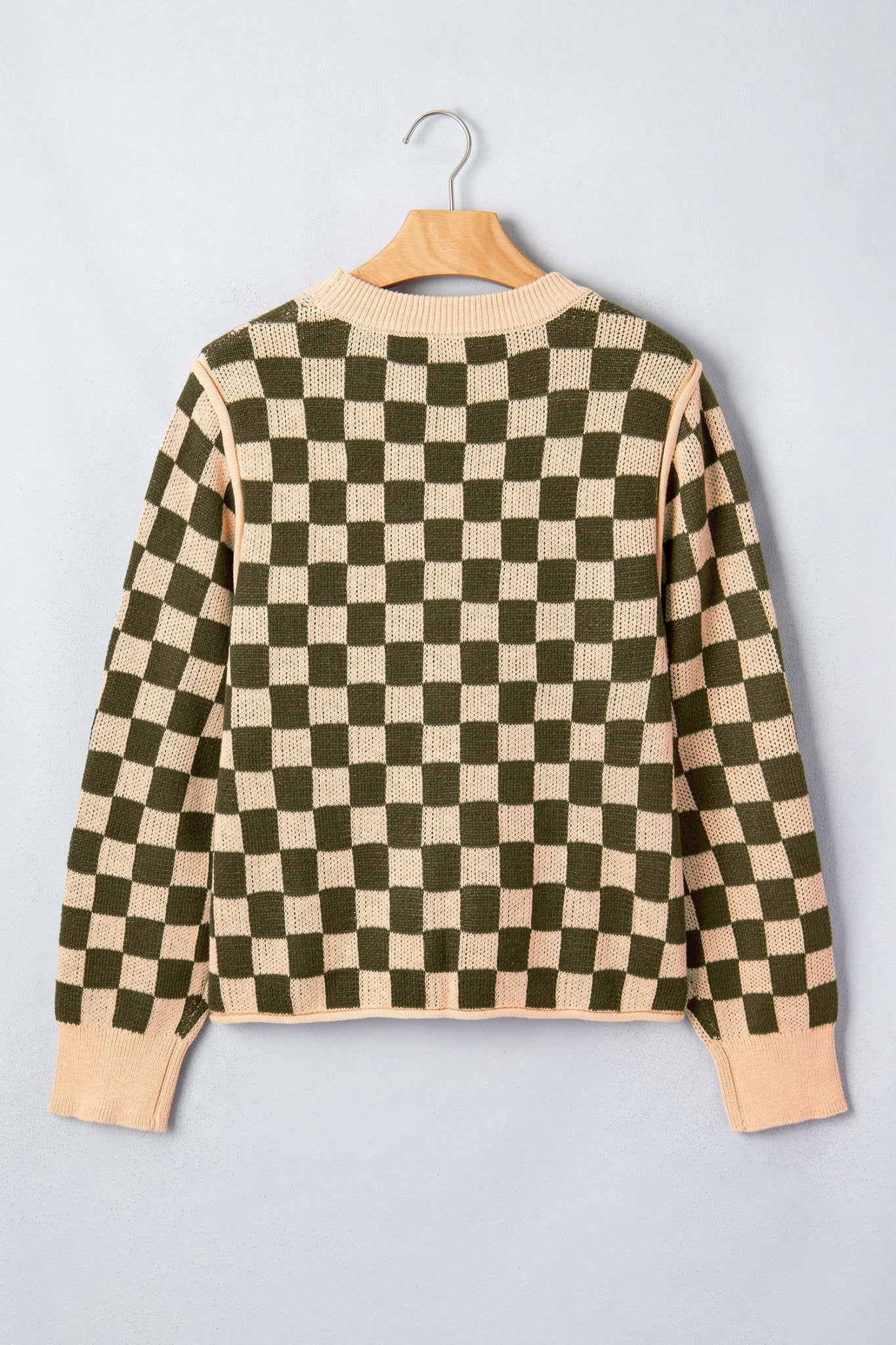 A long-sleeve knit sweater with a checkered pattern hanging on a wooden hanger.