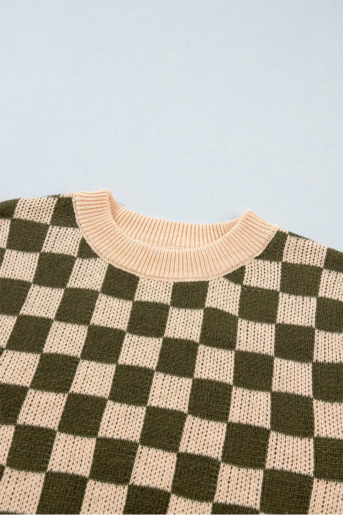 Close-up of beige and dark olive green checkerboard knit sweater with ribbed light beige crew neck.