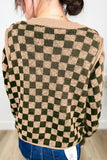 Back view of a person in an olive green and beige checkerboard knit sweater.