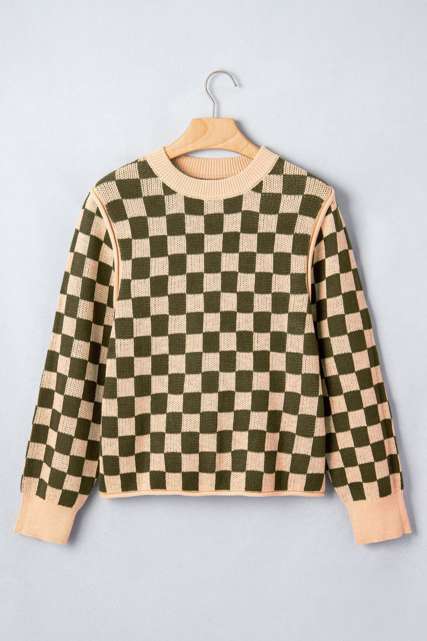 A long-sleeve crewneck sweater with a green and beige checkerboard pattern, hanging on a wooden hanger.