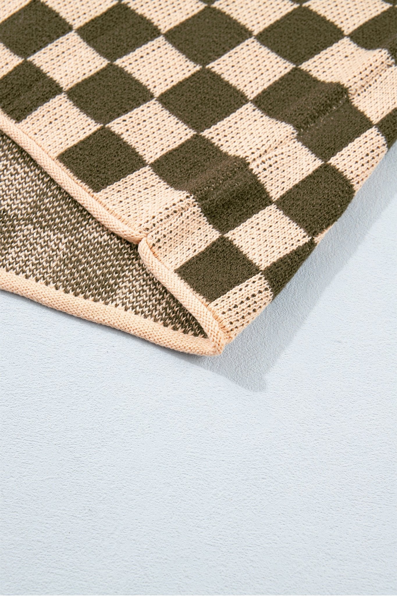 Close-up of folded woven textile featuring a dark olive green and beige checkerboard pattern.