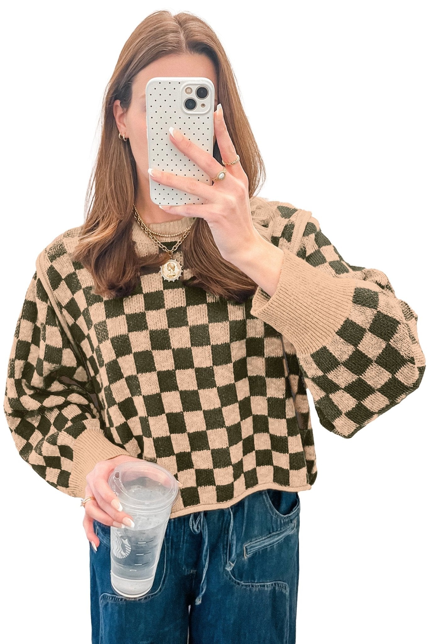 Woman taking a mirror selfie in cropped dark olive green and beige checkerboard knit sweater with jeans.