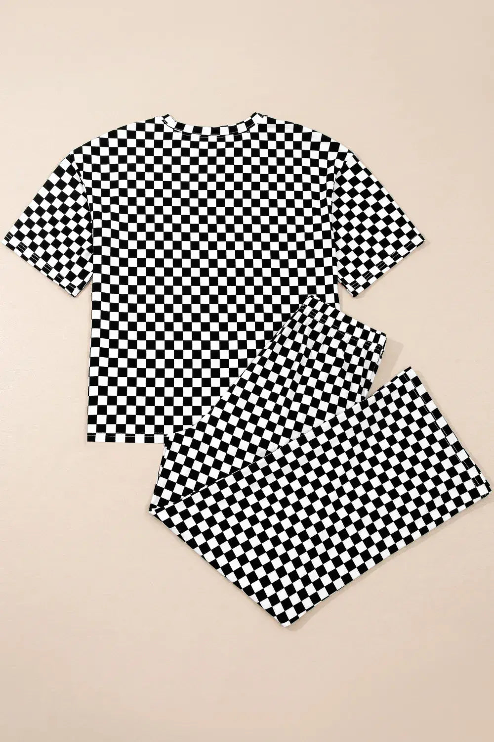 A matching short-sleeve top and shorts set with a bold black and white checkerboard pattern, laid flat on a solid beige background.