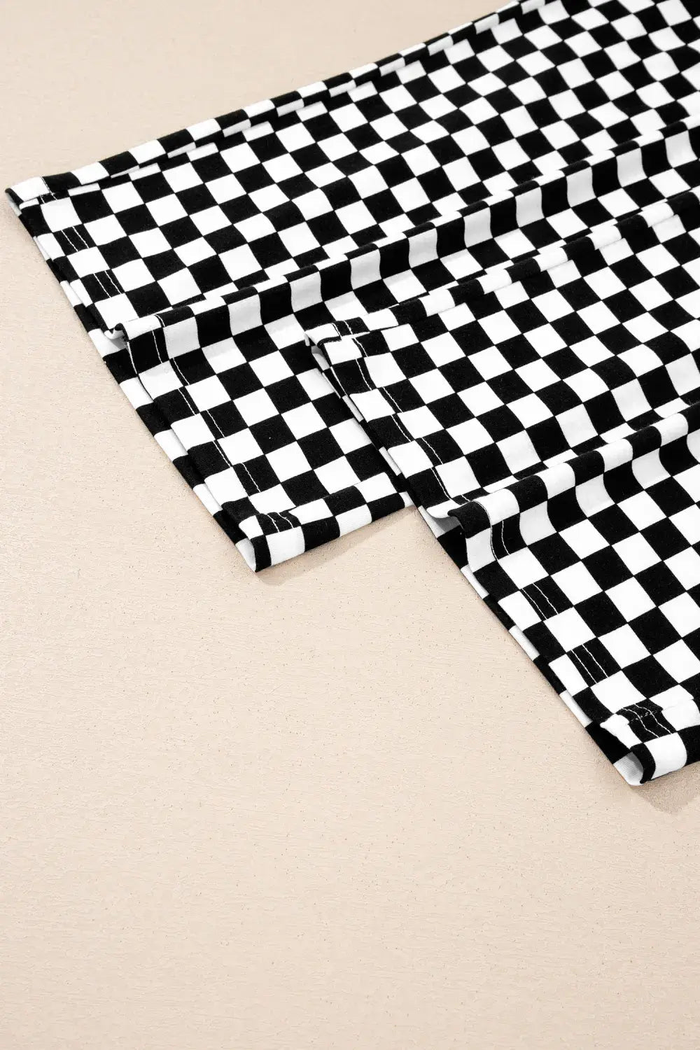 A close-up of a black and white checkerboard patterned fabric laid flat on a light beige background.