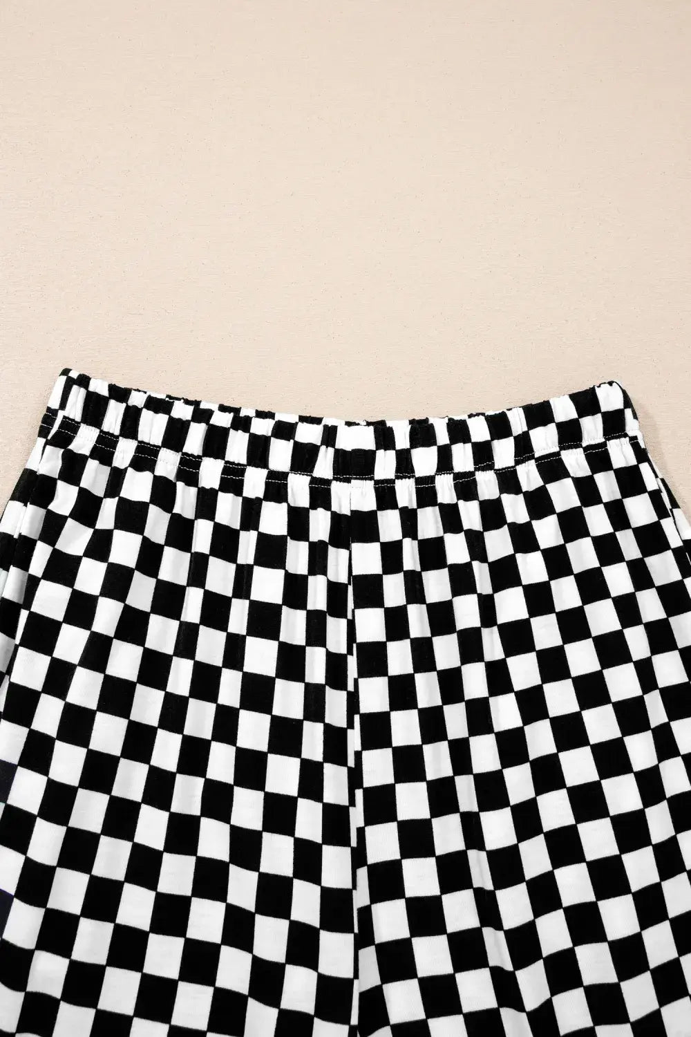 Black and white checkered patterned shorts shown from the waist down on a solid beige background.
