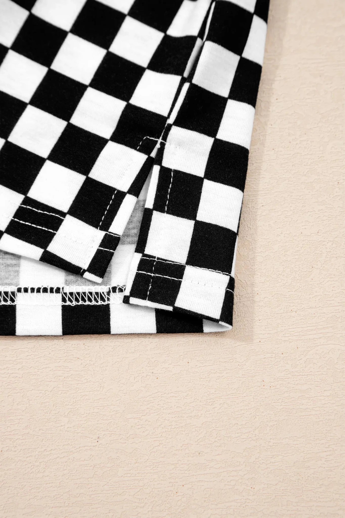 A close-up of a black and white checkered fabric, showing the texture, stitching, and folded edges, set against a light beige background.