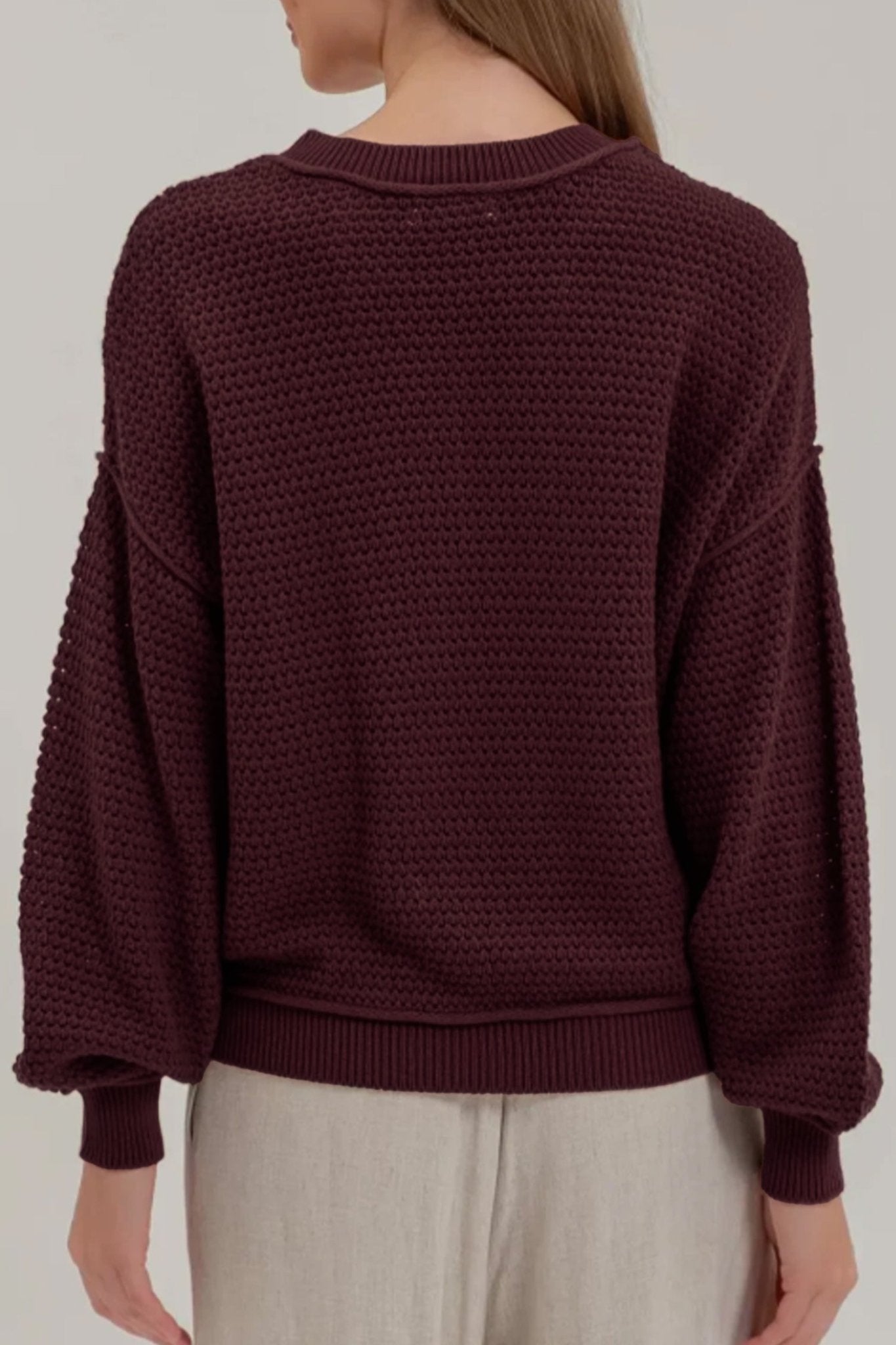 Back view of woman in deep burgundy waffle-knit sweater with light beige trousers.