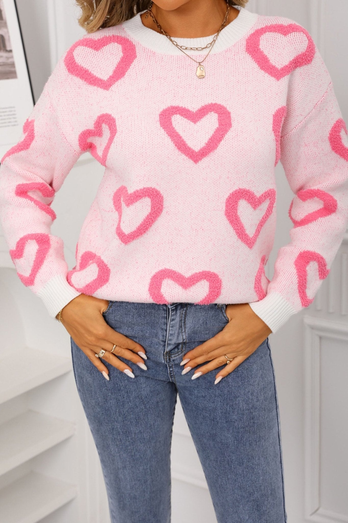 Person wearing a pink sweater with heart patterns and blue jeans indoors.