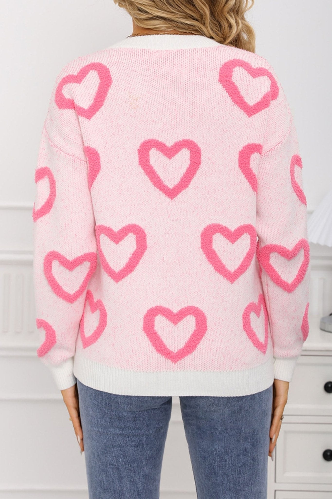 Pink sweater with heart patterns worn by a person, against a neutral background