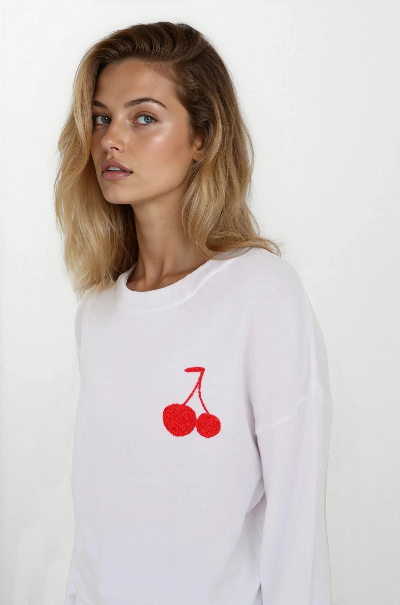 Woman wearing a white sweatshirt with red cherry design on a plain background
