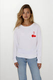 Woman wearing a white sweatshirt with red cherry design on a plain background
