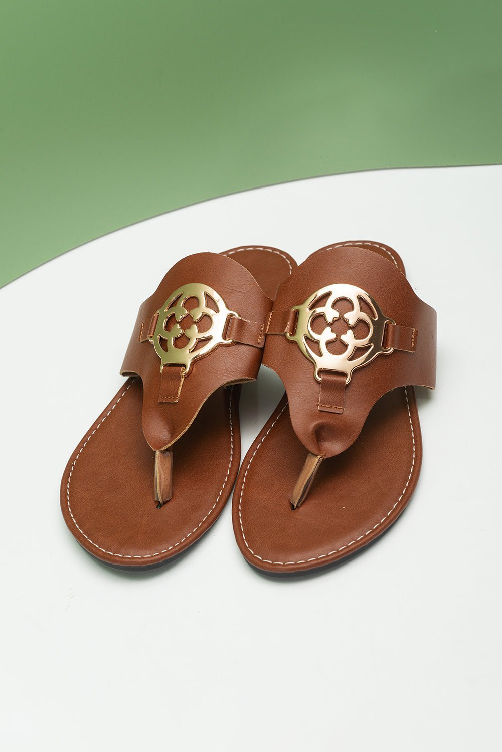 Pair of brown sandals with gold embellishments on a white surface with a green background