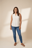 Woman wearing a white sleeveless blouse and blue jeans against a beige background