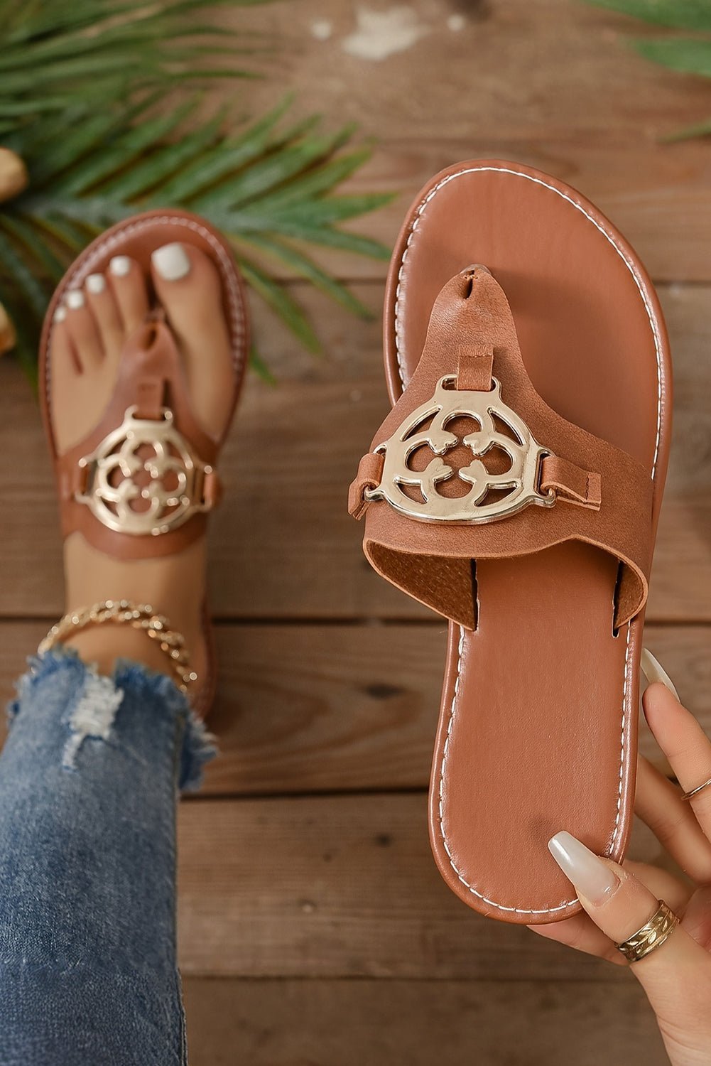 Brown sandals with gold embellishments on a wooden floor
