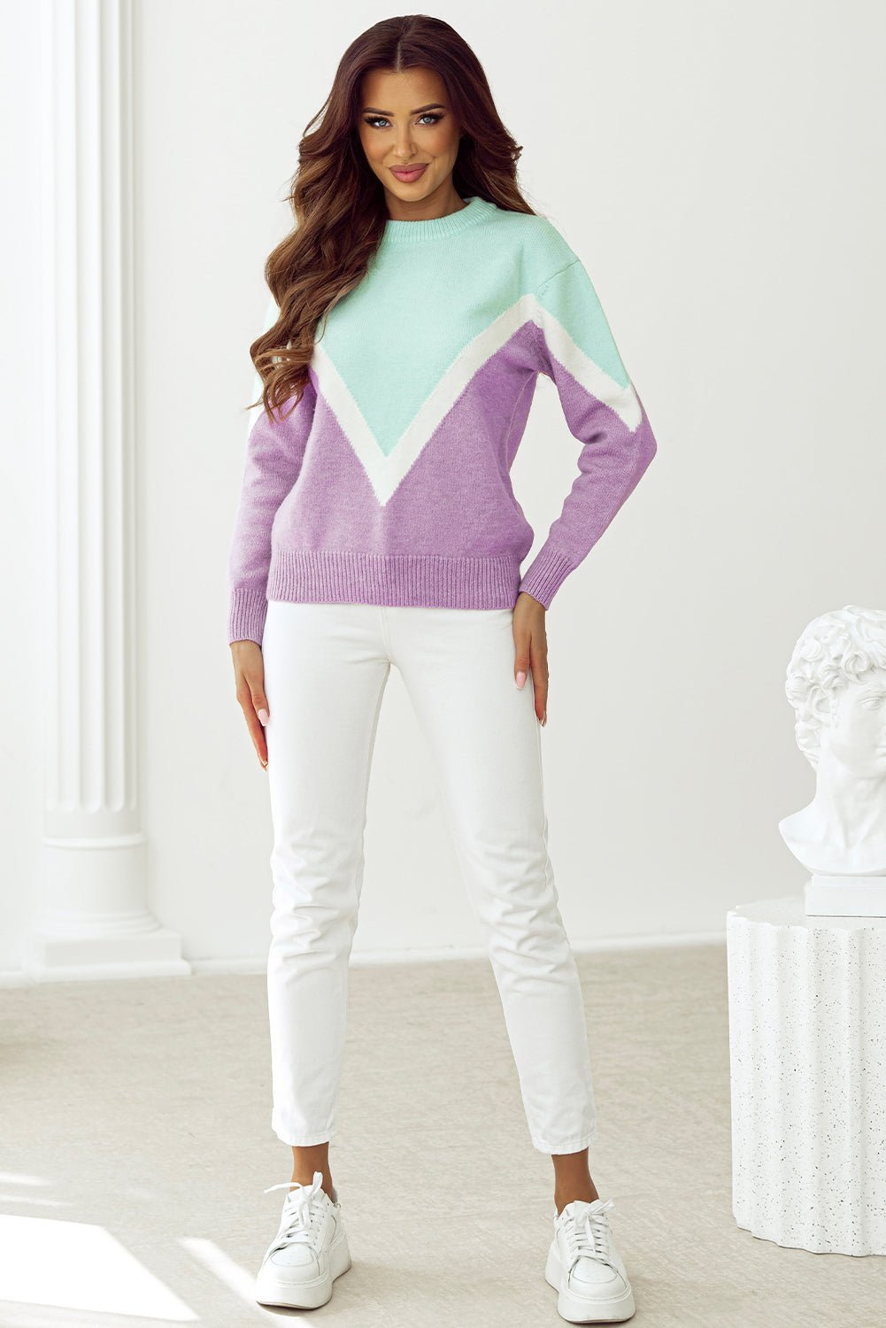 Woman wearing a colorful sweater and white pants in a minimalistic setting