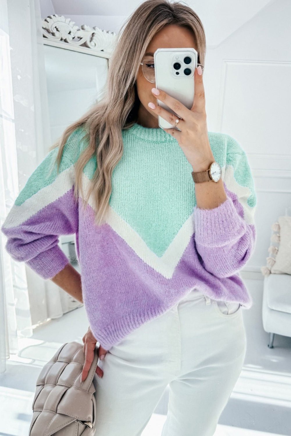 Woman wearing a colorful sweater taking a selfie in a bright room.