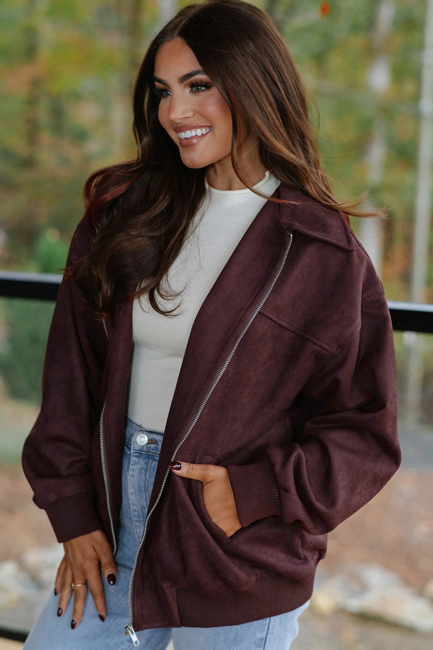 Woman wearing chicory coffee collared bomber jacket with a cream top and light wash jeans