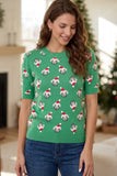 Woman in green knit sweater with Santa-hat dog pattern and blue jeans.