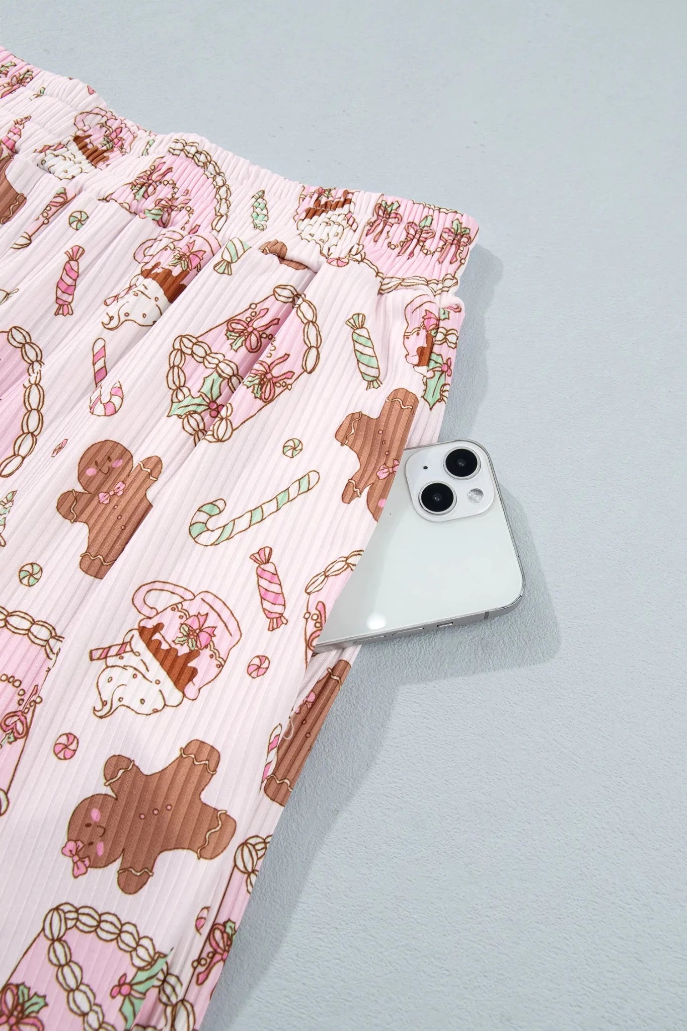 Close-up of pink striped pajama pants with gingerbread print and white smartphone.