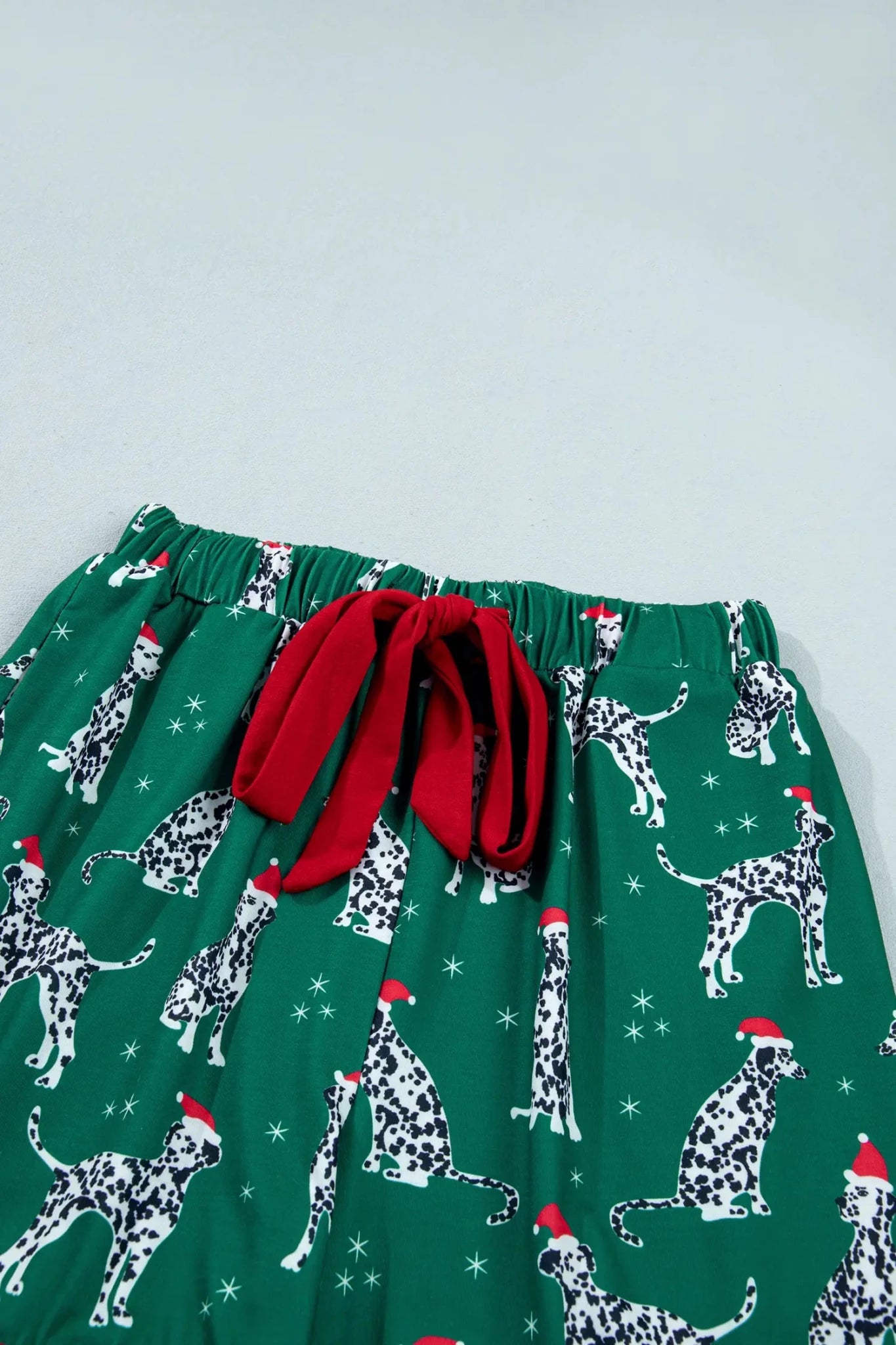 Green Dalmatian holiday pants with Santa hats, snowflakes, and red bow.