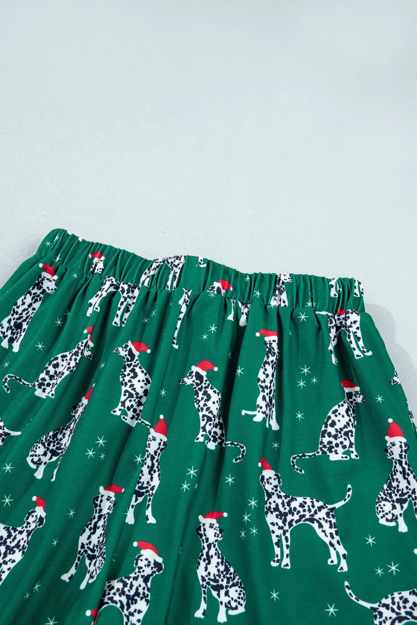 Green elastic waist skirt with a repeating pattern of Dalmatian dogs wearing red Santa hats and white snowflakes.