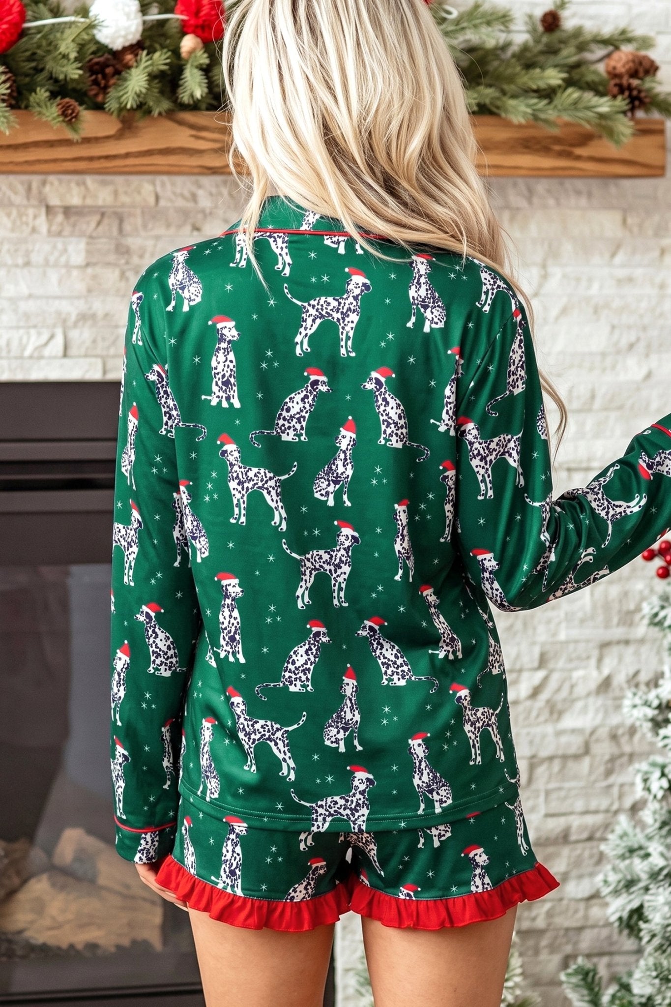Woman in green Dalmatian-print pajamas with red ruffle trim, standing by a fireplace.