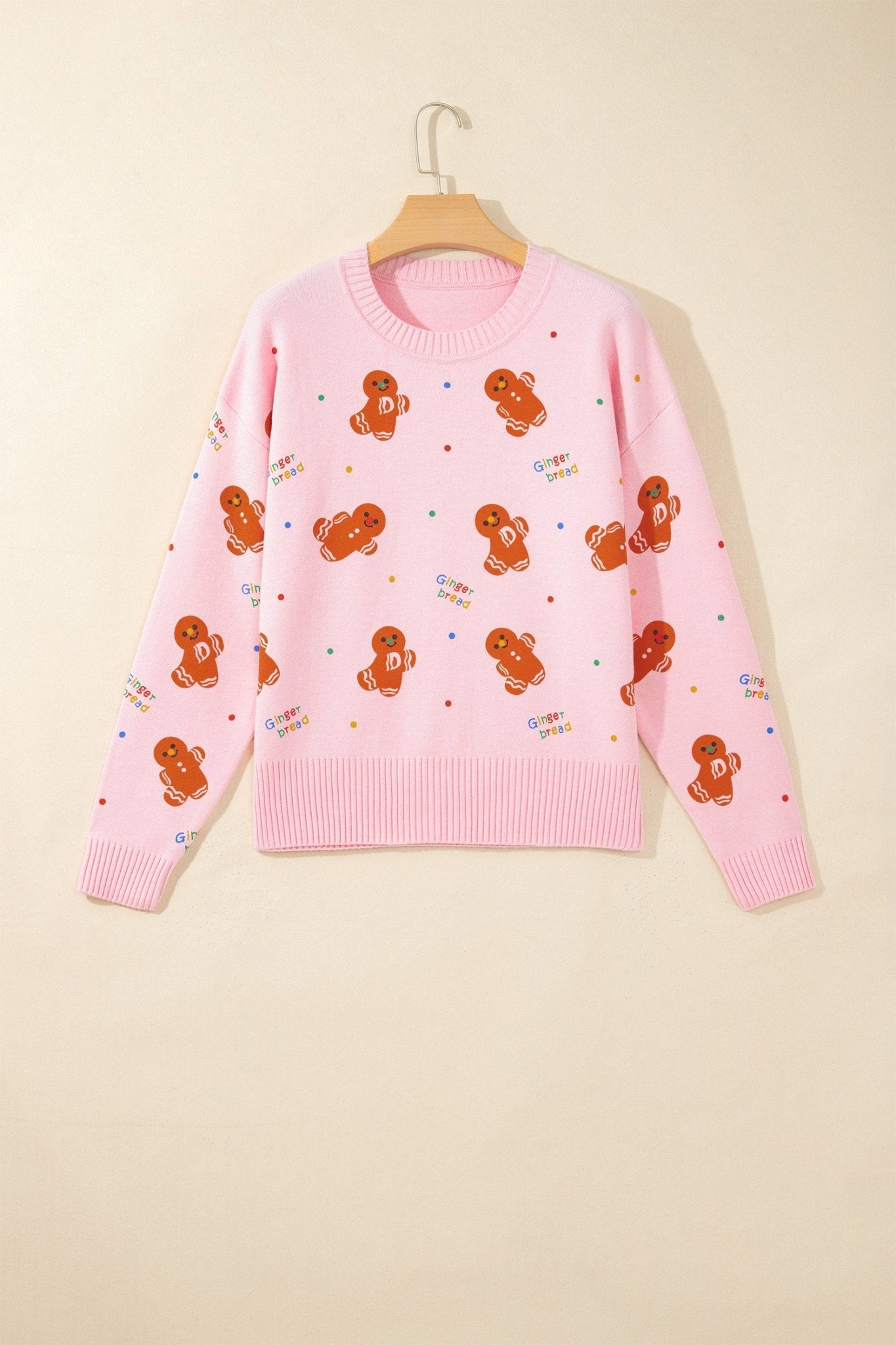 Pink knit sweater with gingerbread pattern and colorful details on wooden hanger.