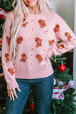 Woman in light pink gingerbread-pattern sweater with dark blue jeans by Christmas tree.