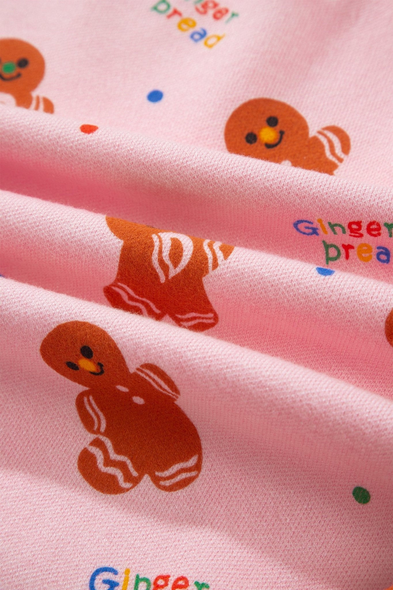 Pink fabric with repeating gingerbread print and multicolored text accents in soft folds.