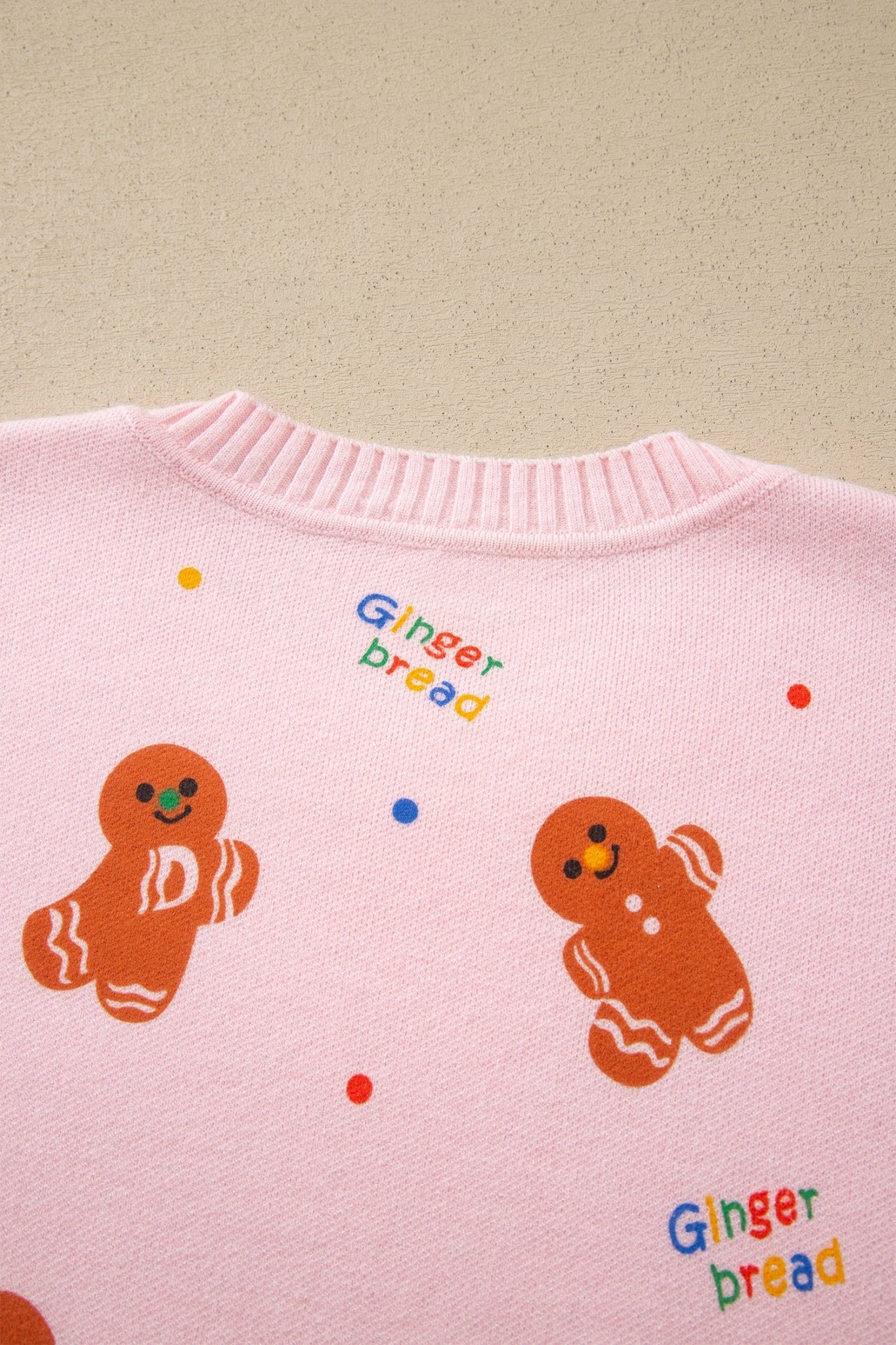 Close-up of pink knit sweater with gingerbread illustrations and colorful lettering.