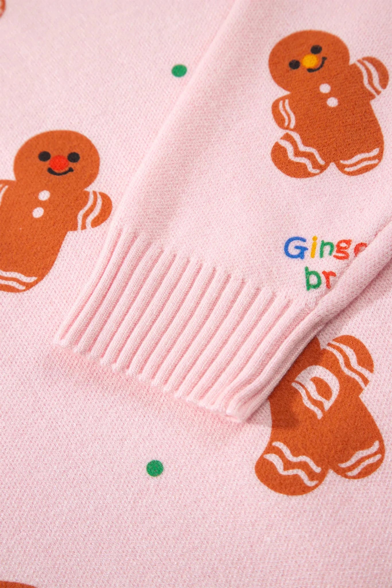 Close-up of pink knit sweater with gingerbread prints, green dots, and ribbed cuff.