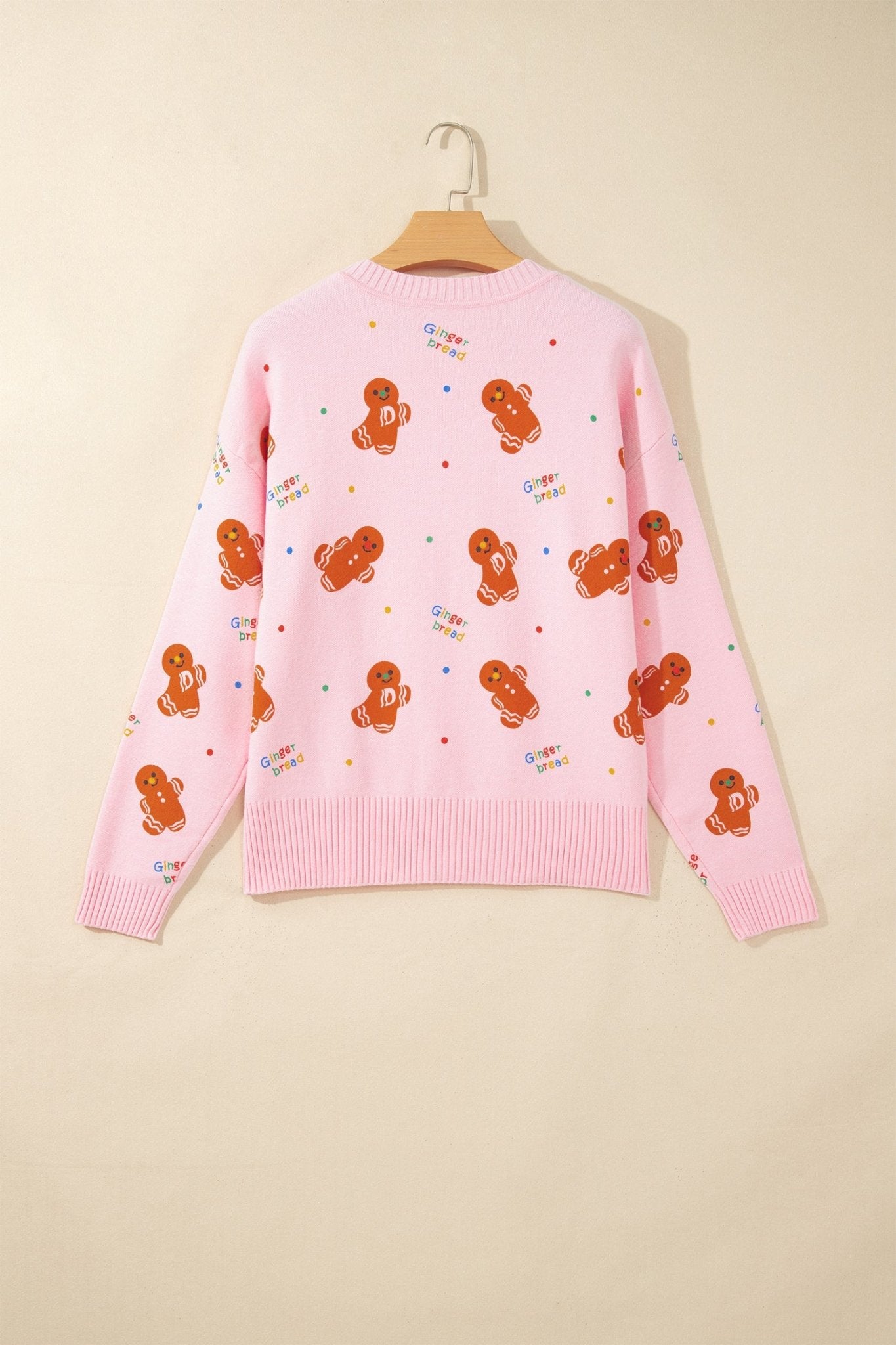 Pink knit sweater with gingerbread print and colorful text accents on hanger.
