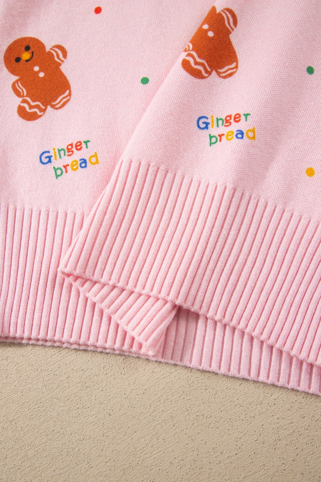 Close-up of pink knit garment with ribbed cuffs, gingerbread prints, and letter.