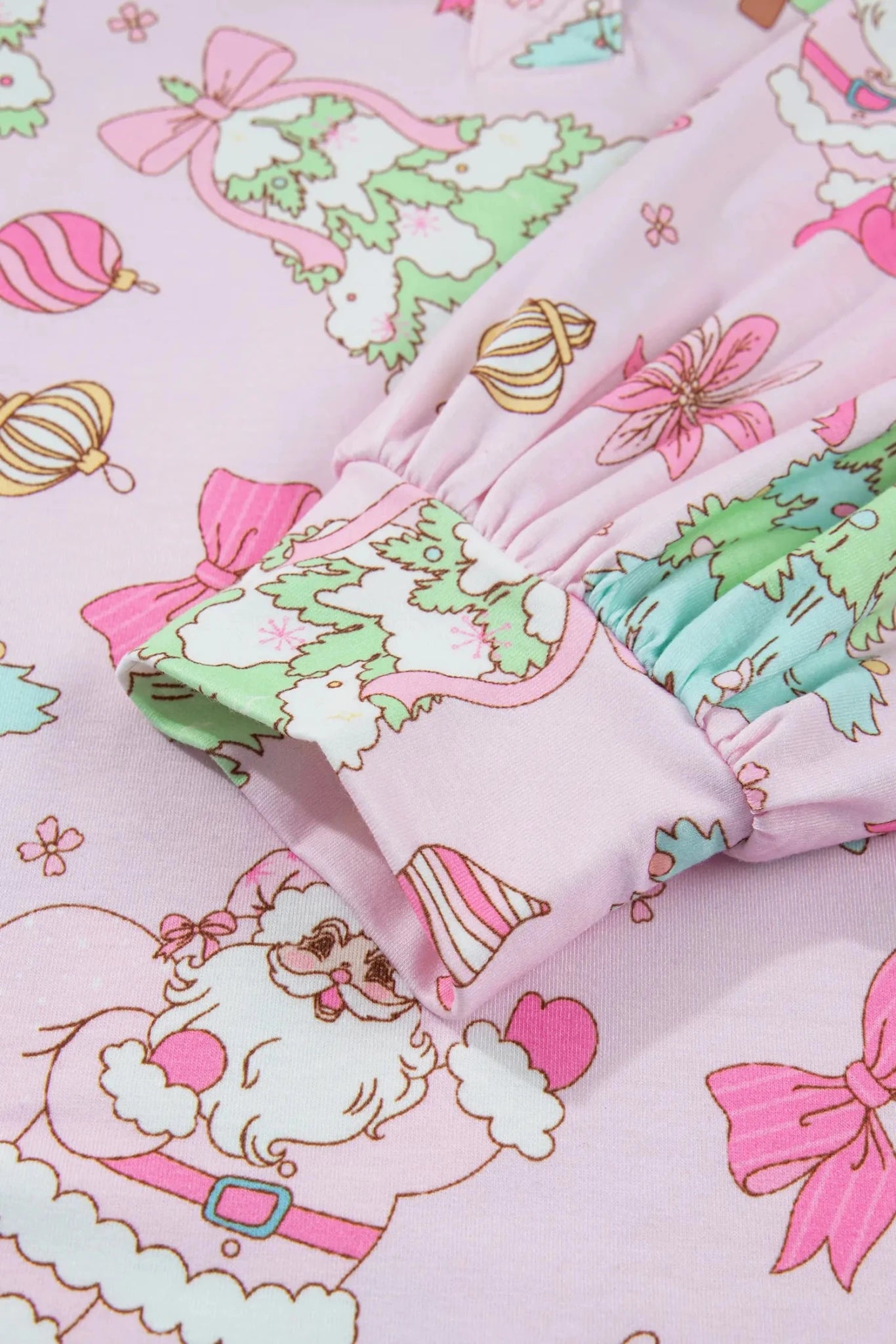 Close-up of light pink Christmas-print fabric with Santa, bows, and trees.