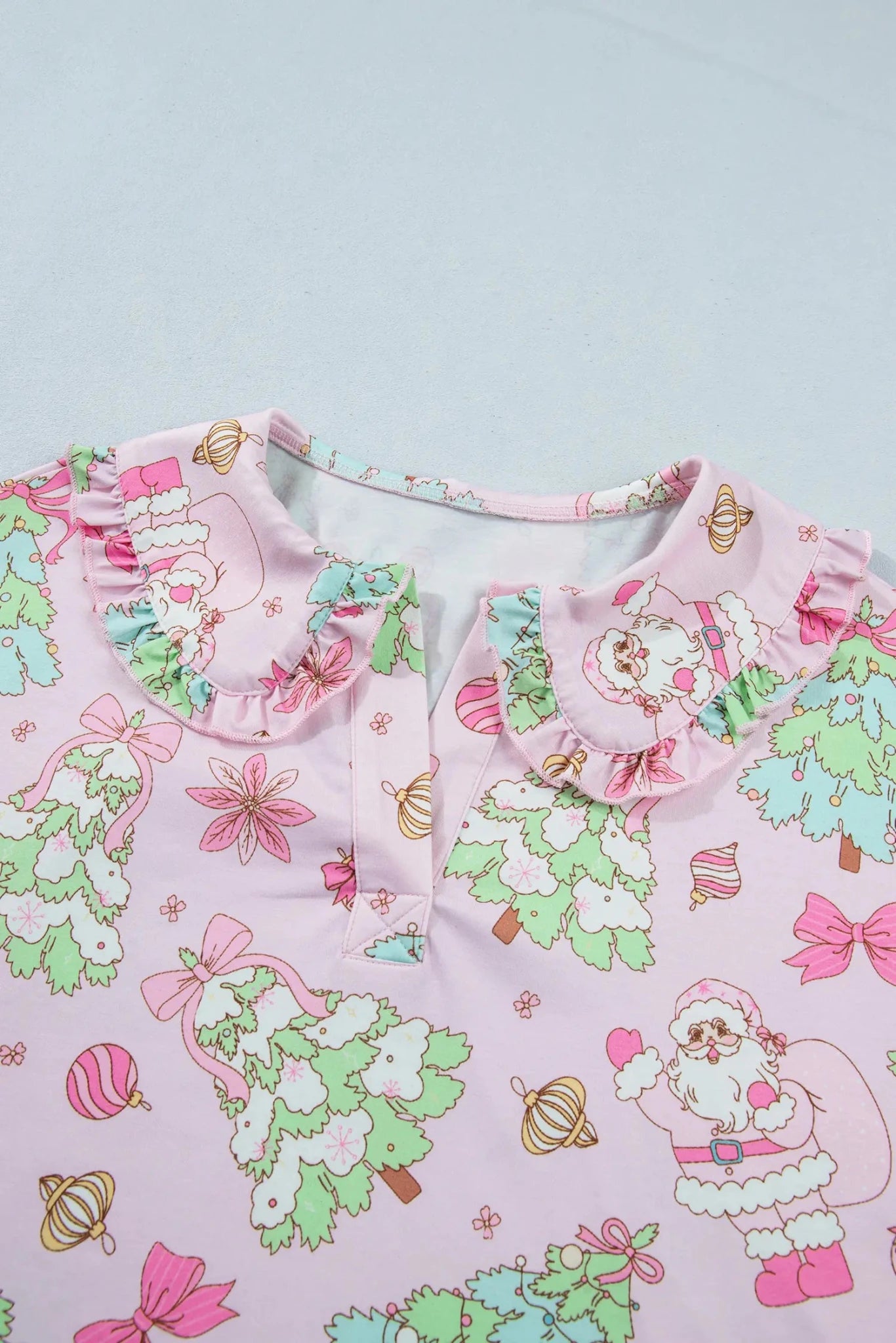 Close-up of pink Christmas-print top with ruffled collar and button front.
